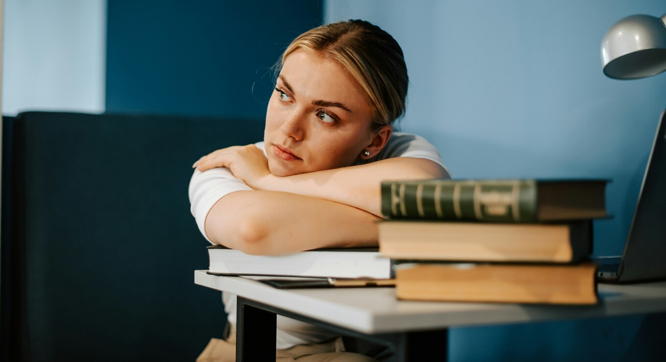 Denkende Frau vor Bücherstapel