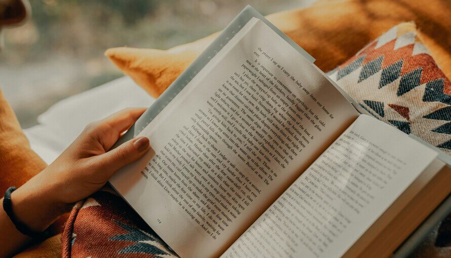 Frauenhand hält ein aufgeschlagenes Buch mit gut sichtbaren Buchseiten.